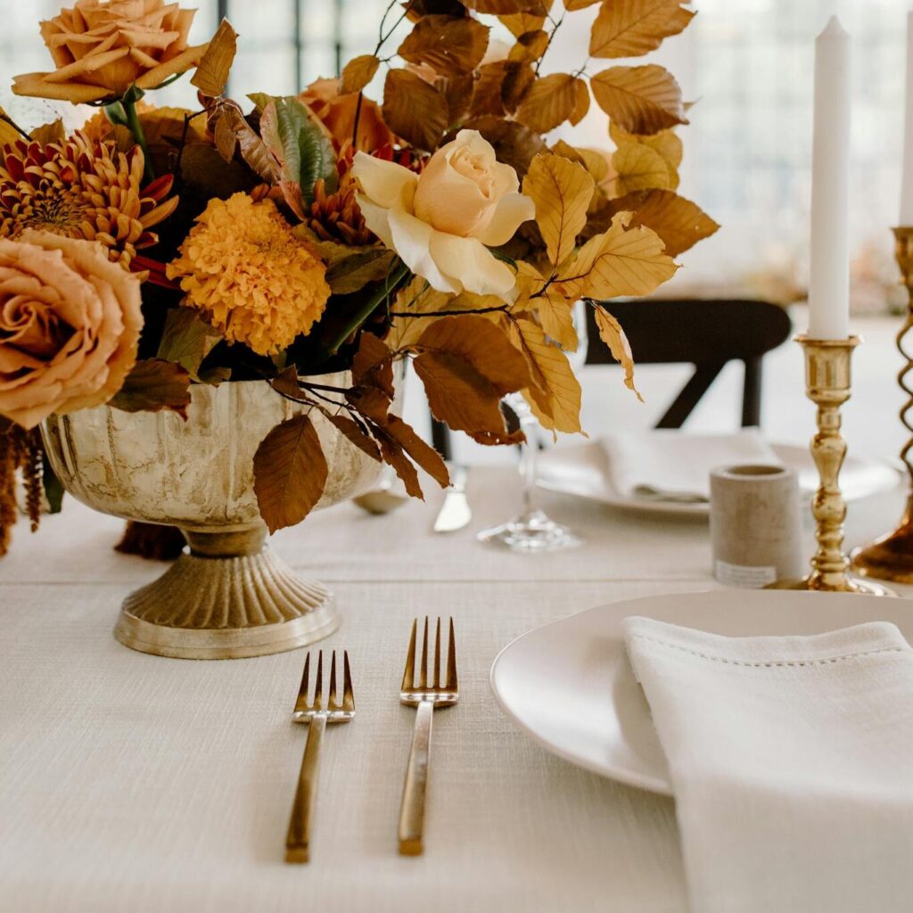 Elegant floral composition in vase placed on white table with ceramic plates and golden cutlery during festive banquet